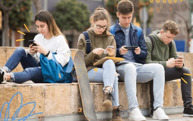 czwórka nastolatków ze smartfonami siedzi na murku
