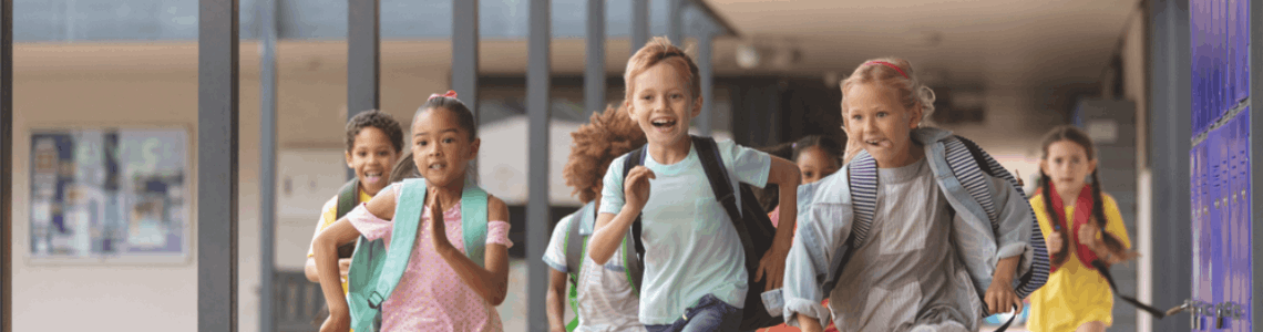 dzieci w wieku szkolnym biegną uśmiechnięte na tle szkoły